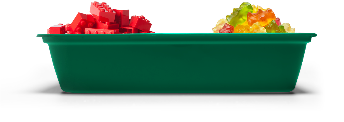 A green tray with red toy building blocks on the left and colorful gummy bear candies on the right.